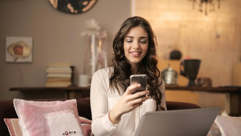 A woman enjoying leisure time using her smartphone and laptop in a cozy living room.